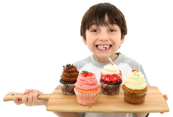 Criança sorrindo e segurando uma tábua com cupcakes - Foto: Jaimie Duplass / ShutterStock