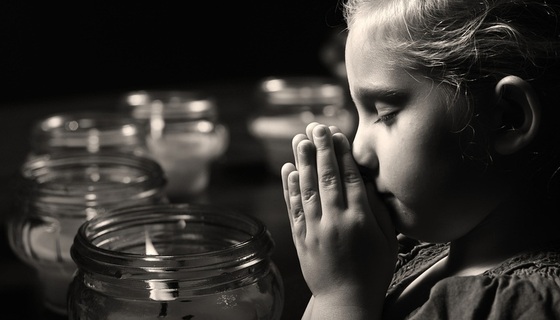 Criança fazendo uma oração cercada de potes com velas acesas - Foto: itsmejust/ShutterStoc.com