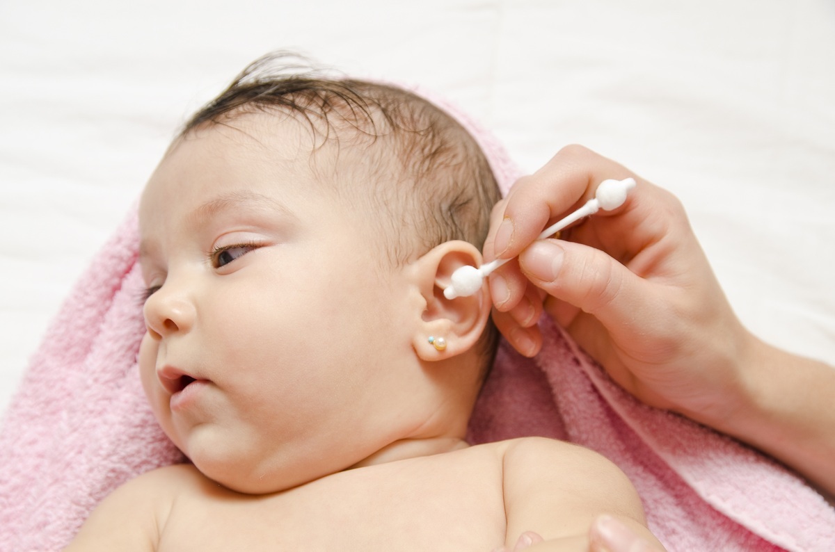 Mãe limpando a orelha do bebê com hastes de algodão com barreira protetora - foto: maxriesgo/ShutterStock.com