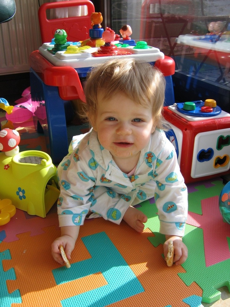 Criança sentada no tapete rodeada de brinquedos e com biscoito na mão - foto: chris vdh/FreeImages.com