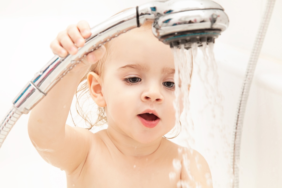 Bebê tomando banho segurando a ducha - foto: Mahony/ShutterStock.com