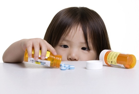 Criança com um pote de remédio aberto e despejando os comprimidos sobre a mesa - Foto: Thomas M Perkins/Shutterstock.com