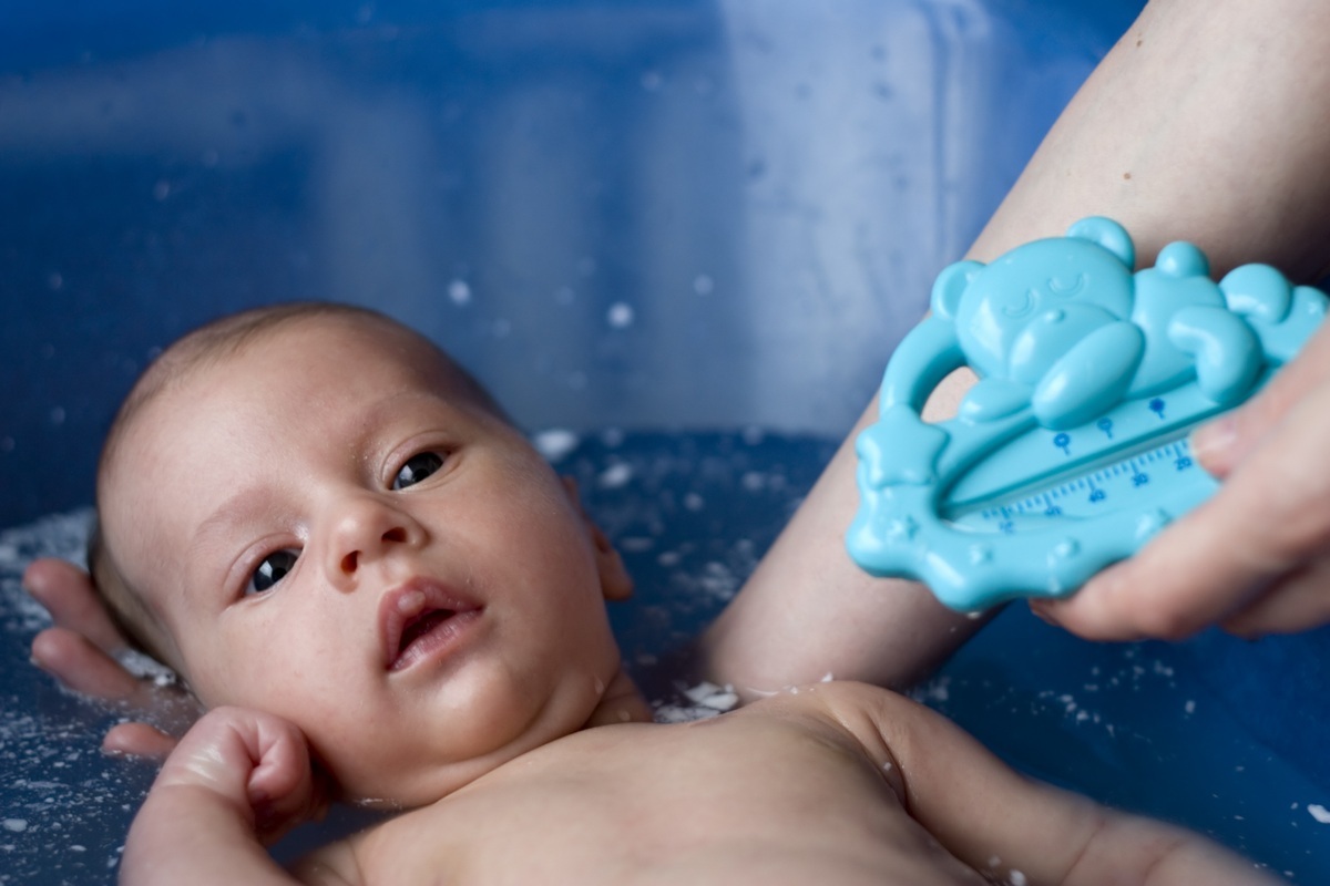 Bebê na banheira segura pela mãe que verifique o termômetro - foto: Szente A/ShutterStock.com