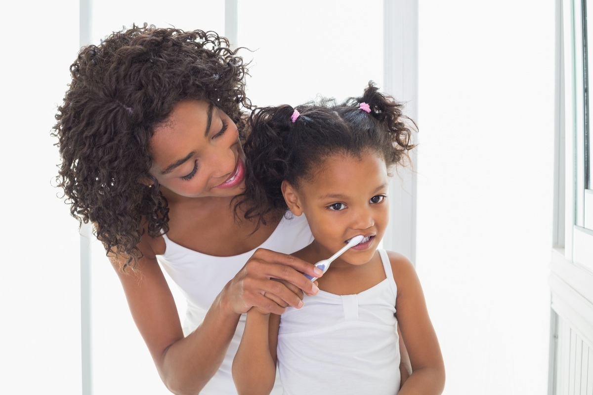 Mãe ensinando a filha a escovar os dentes - foto: wavebreakmedia/ShutterStock.com