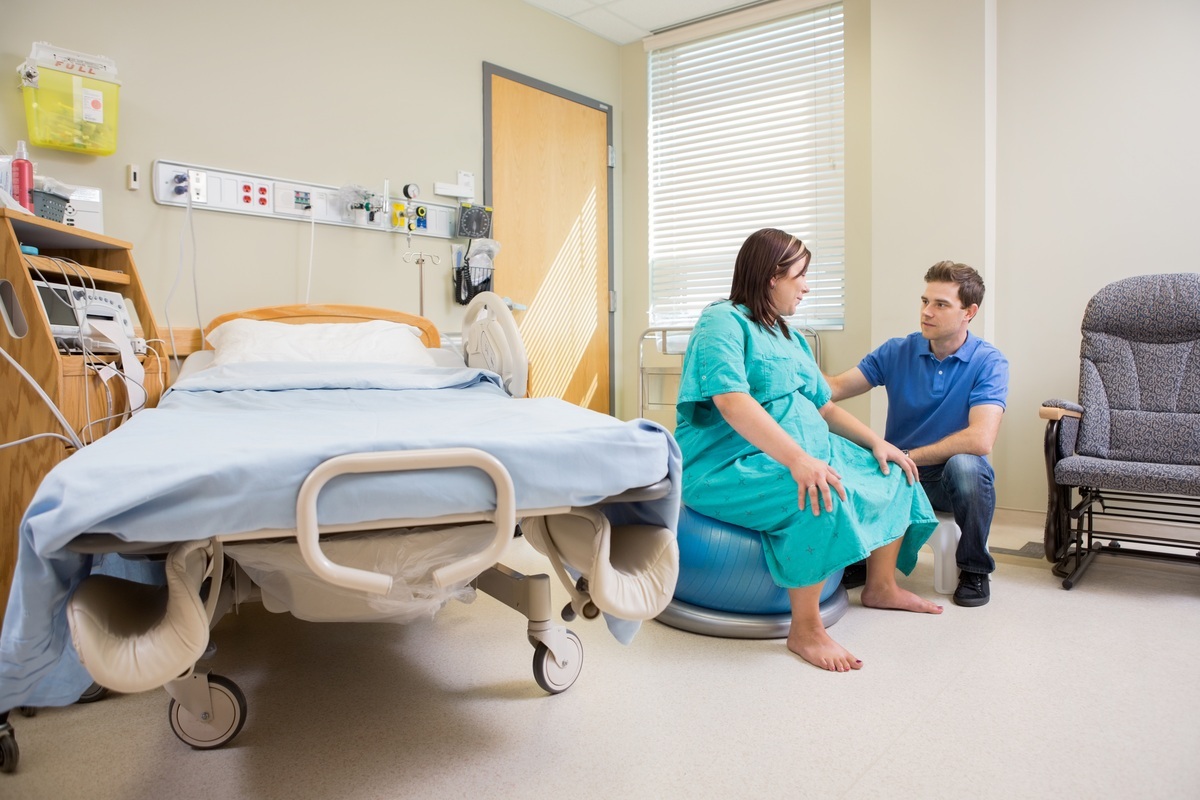 Mulher no quarto do hospital sentada em uma bola de exercícios ao lado de seu marido - foto: Tyler Olson/ShutterStock.com
