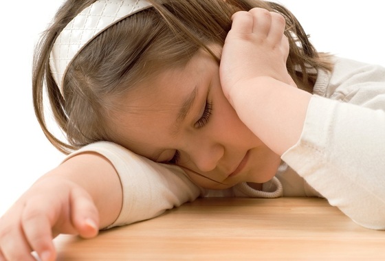 Criança aparentando cansaço ou sonolência debruçada sobre a mesa - Foto: dragon_fang/Shutterstock.com