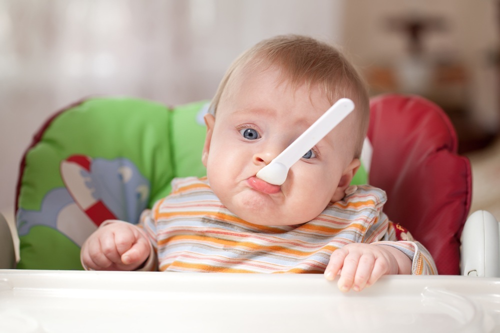 Bebê com colher na boca fazendo cara de triste - foto: gresei/ShutterStock.com